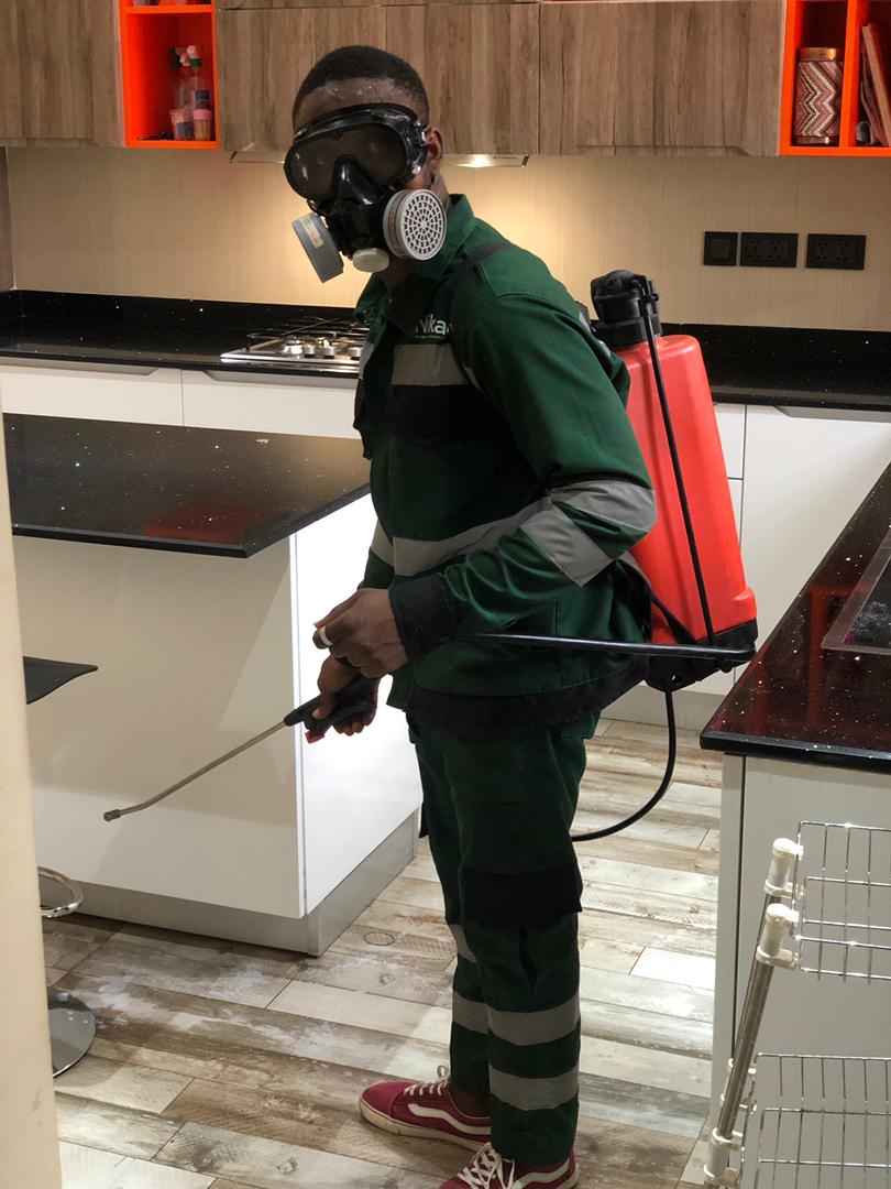 Technician fumigating a kitchen with a backpack sprayer in Ghana